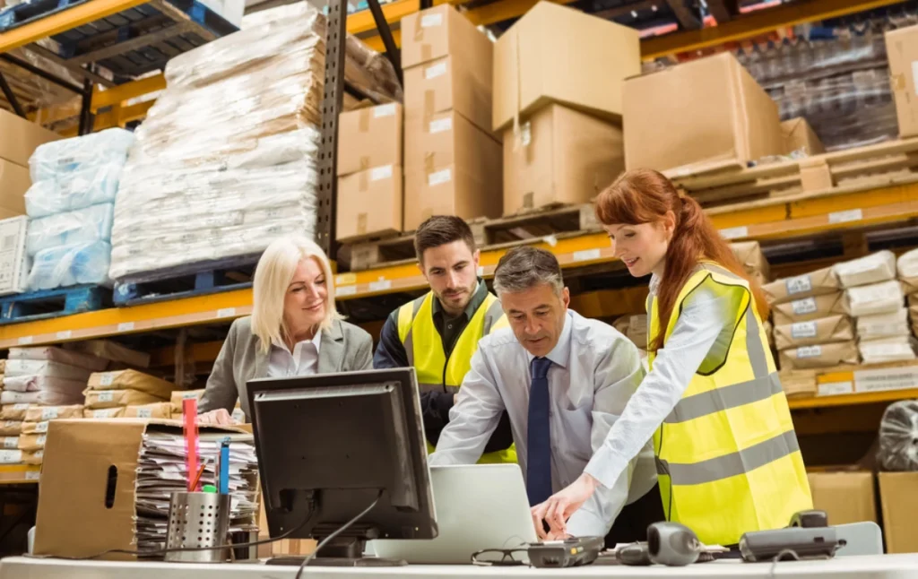 a warehouse, three people analyse data, focusing on improving supply chain resilience strategies.
